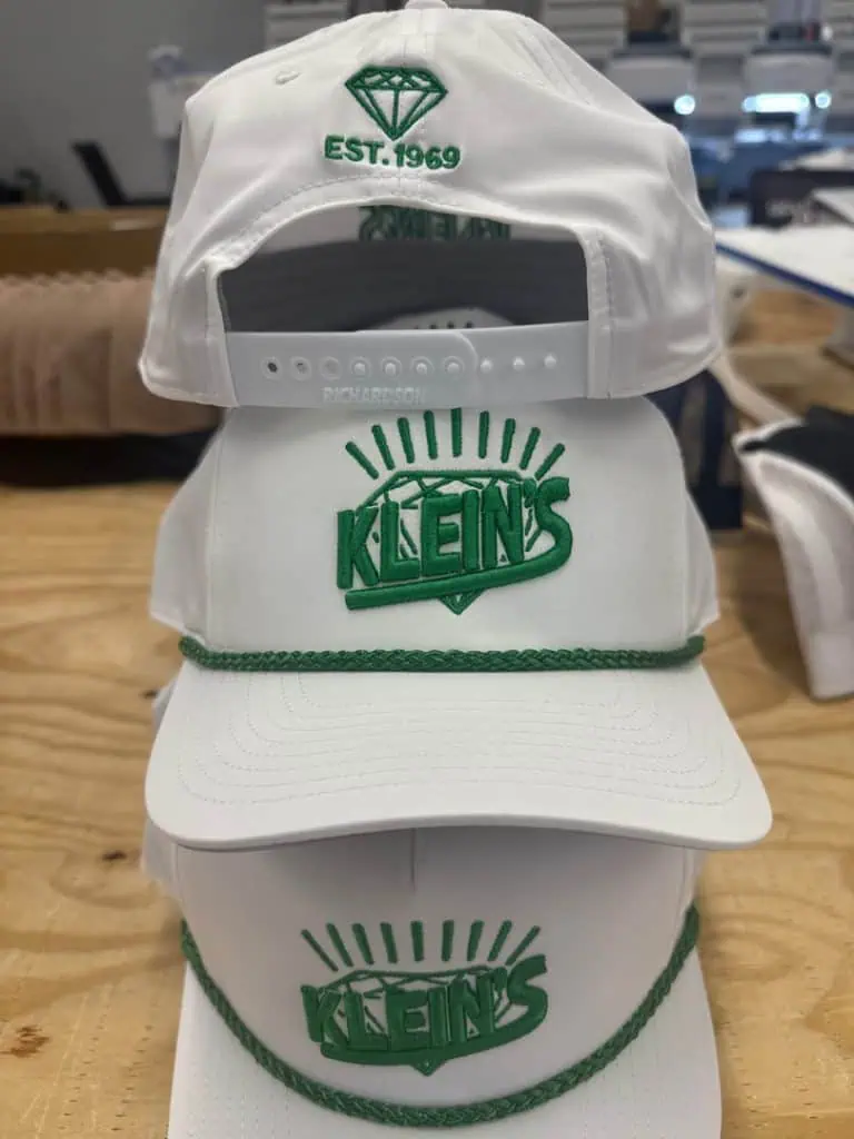 White Klein's cap with green logo and sunburst design, adjustable strap, and embroidered details.